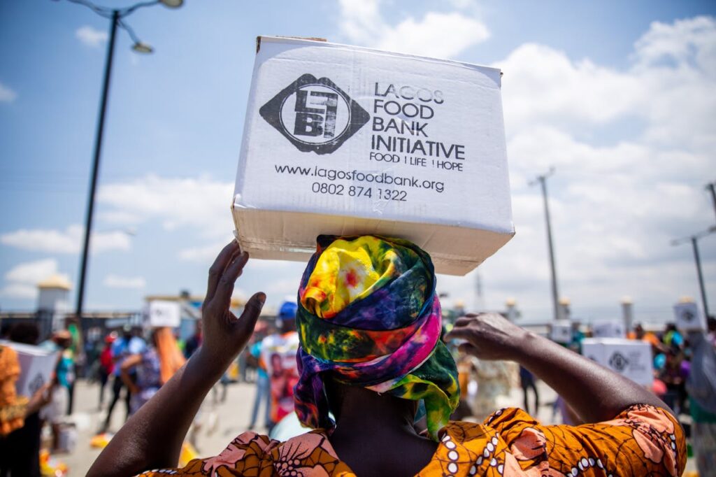 A woman in colorful attire carries a donation box from Lagos Food Bank Initiative.